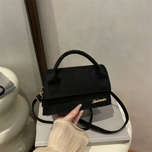 French style black matte crossbody bag with gold logo being held in minimalist setting