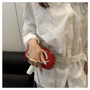 Detail of red patent leather shoulder bag with bold gold U-shaped handle and chain strap