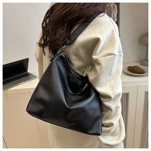 Detail of black textured faux leather tote bag with wide strap and gold hardware accents