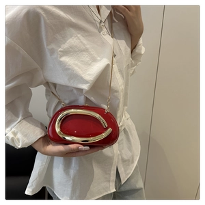 Detail of red glossy shoulder bag with gold C-shaped buckle and fine chain strap