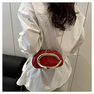 Detail of red patent leather shoulder bag with bold gold metal accent and chain