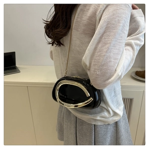Chic black patent leather crossbody bag with gold metal oval ring worn by a model