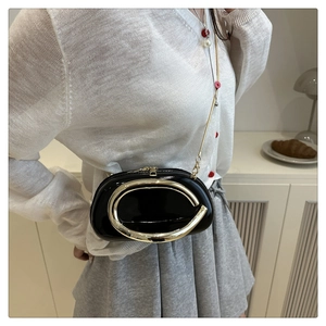 Detail view of black patent leather bag with a gold metal ring and chain strap