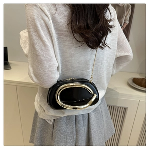 Detail of a black patent leather crossbody bag with a large gold C-shaped metal buckle