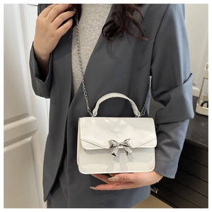 Detail of white mini crossbody bag featuring a silver bow buckle and metal chain strap