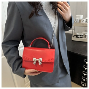 Detail of red PU leather bag with silver bow ornament and chain strap on grey blazer