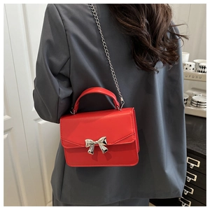 Detail of red square crossbody bag with silver bow accent and metal chain strap