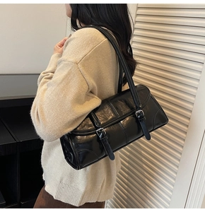 Detailed view of black glossy shoulder bag with silver buckles on beige sweater