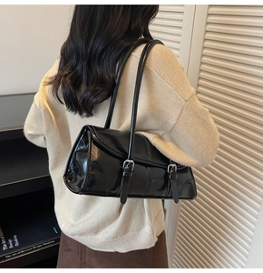 Close-up of black glossy faux leather shoulder bag with silver metallic buckle detail