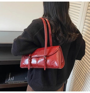 Detail of burgundy glossy leather shoulder bag worn by model over a black sweater