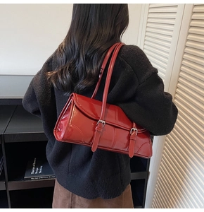 Detail of red glossy shoulder bag with dual straps and buckle design in a studio setting