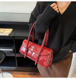 Detail of red glossy leather shoulder bag with metallic buckles on a model
