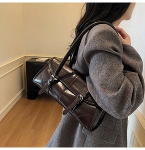 Close-up of a dark brown glossy leather shoulder bag with buckle details and silver hardware