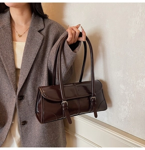 Detail of dark brown glossy leather baguette bag with decorative buckle straps