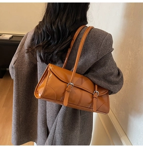 Detail of glossy orange-brown leather shoulder bag with double strap and flap closure