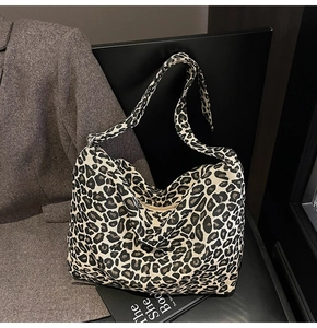 Large leopard print canvas hobo bag placed on a black leather chair with modern decor