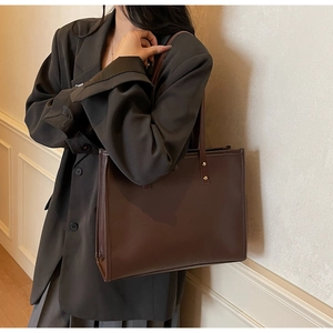 Detail of dark brown leather tote bag with gold rivets shown on a stylish model