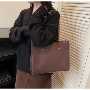Detailed view of dark brown leather tote bag with gold rivets and magnetic snap closure