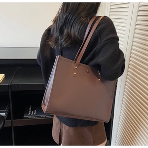 Close-up of a large brown leather tote bag with slim shoulder straps and metal rivets