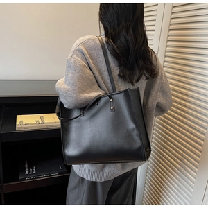 Woman in grey sweater carrying a large black vintage leather tote bag for commuting
