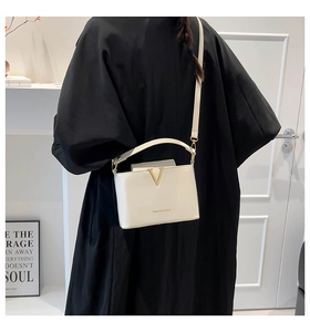 Detail of white leather crossbody bag with V-shaped gold metal clasp on black jacket