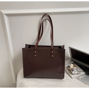 Detail view of large dark brown leather tote bag with long straps and gold rivets