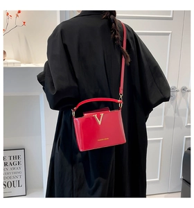 Detail of red glossy shoulder bag featuring gold V-logo and sleek fashion strap