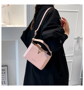 Detailed view of pale pink leather handbag with gold V-shape buckle on a black coat