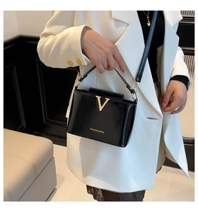 Detail of glossy black patent leather bag with gold V-decoration and fashion logo