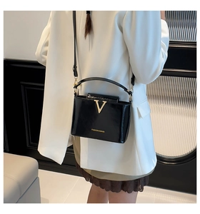 Detail of black patent leather bucket bag with gold V-shape buckle and handle on model