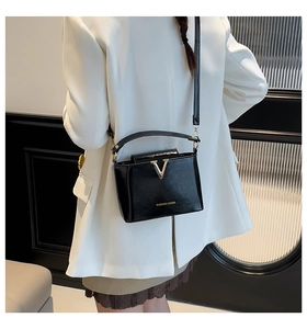 Detail of glossy black leather crossbody bag with iconic gold V-shaped buckle and fine strap