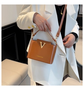 Detail of a brown leather handbag featuring a gold V-shaped buckle and fine stitching