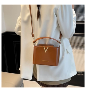 Close-up of brown glossy crossbody bag with golden V-clasp on white blazer jacket