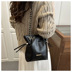Detail of black bucket bag featuring golden chain strap and metallic Fashion logo