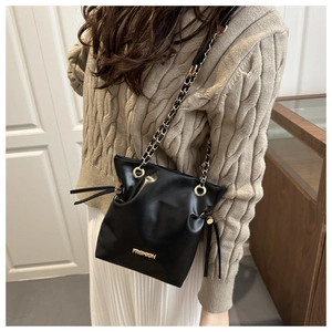 Model wearing a black drawstring bucket bag with gold chain strap and FASHION metal logo