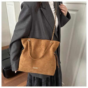 Macro shot of large brown suede bucket bag featuring golden chain and leather straps