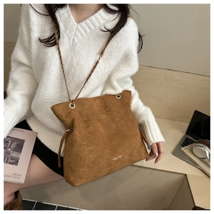 Detailed view of brown suede tote bag with gold chain strap and fashion metal logo