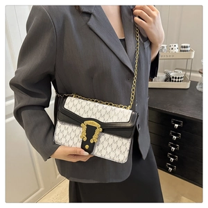 Detail of a chic cream-colored flap bag with M-pattern print and gold clasp on a model