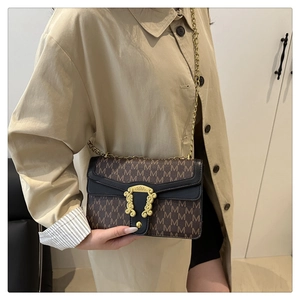 Detail view of a vintage plaid crossbody bag with gold embossed buckle on a beige coat