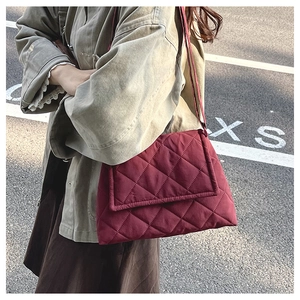 Quilted burgundy shoulder bag with diamond pattern shown on person in a street setting