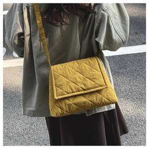 Outdoor shot of a mustard yellow quilted nylon crossbody bag with diamond stitch detail