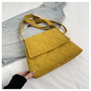 Close-up of yellow quilted nylon crossbody bag with adjustable strap on bed surface