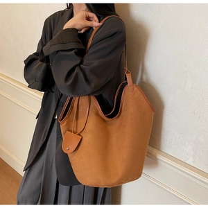 Detail of brown faux suede tote bag featuring reinforced leather edges and side pendant