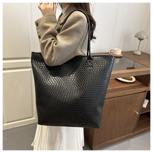 Detail of a large black woven leather tote bag with reinforced shoulder straps and texture