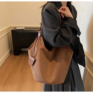 Brown suede tote bag with leather trim and knotted handle detail shown on a model
