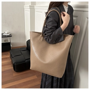 Detail of a large beige tote bag with crocodile texture worn over the shoulder