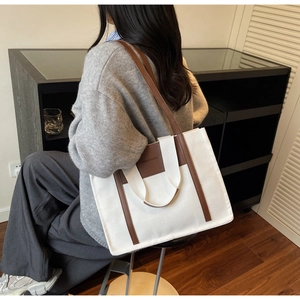 Side view of a large canvas tote bag with brown leather accents worn by a model