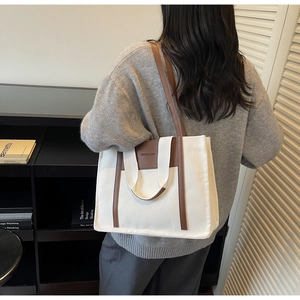 Detail of canvas tote bag with brown leather trim and fashion brand tag on back of model