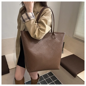 Detail of a large brown tote bag showing intricate woven texture and leather strap