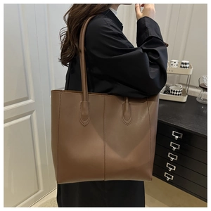 Detail of a brown leather tote bag with vertical stitching and round shoulder handles